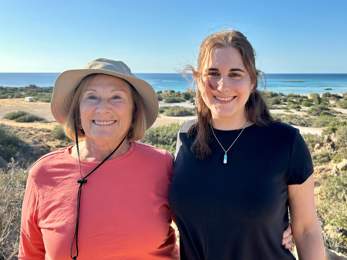 Lorri Bodi and Anna Eglick Bodi smile with vegetated dunes and the ocean behind them.