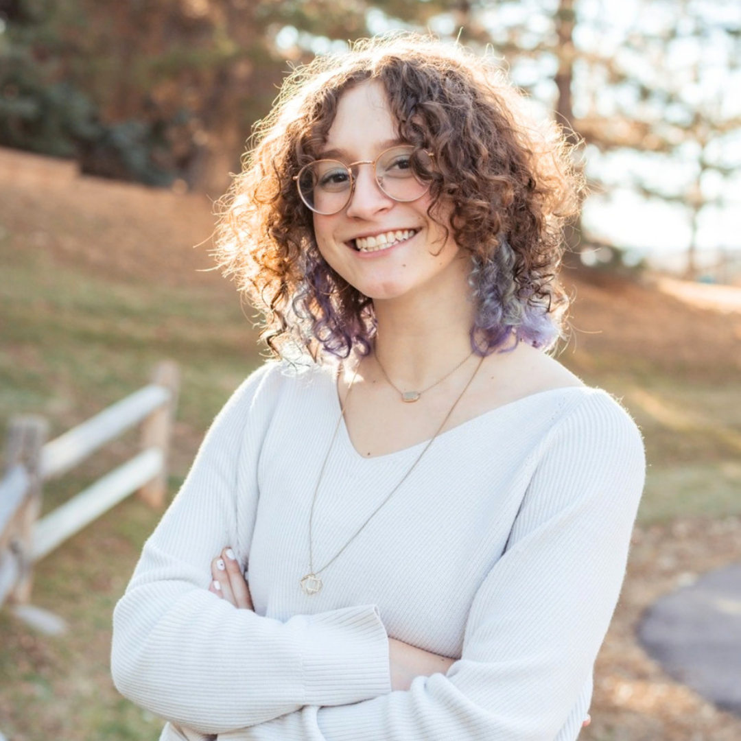 Woman smiles with trees, a fence, and a path behind them.
